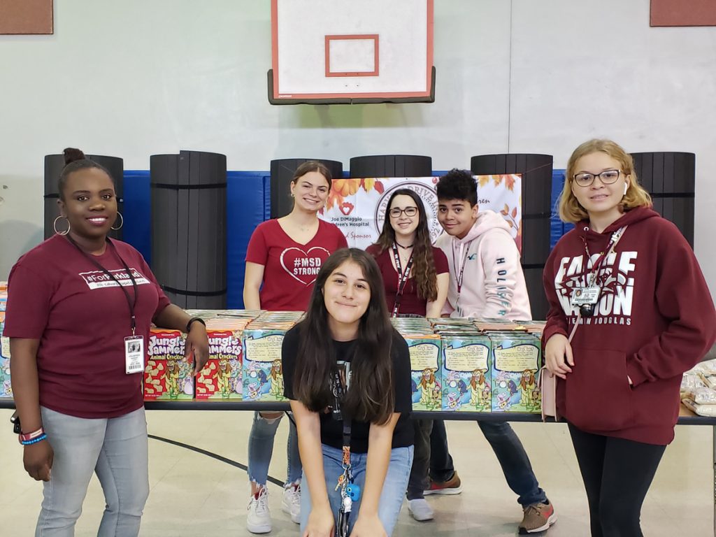 Students standing behind a table of packed food in a school gym