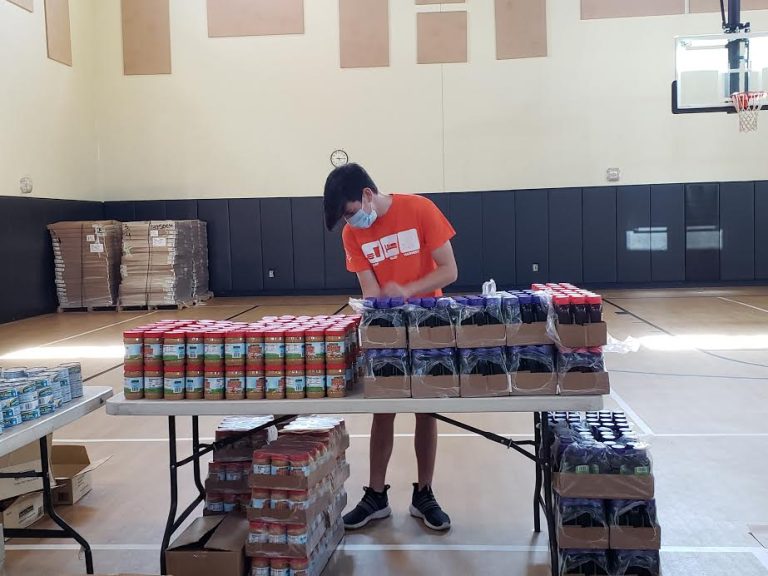 Masked teen lining up canned goods on a table in a gym at Monthly Bag Packings