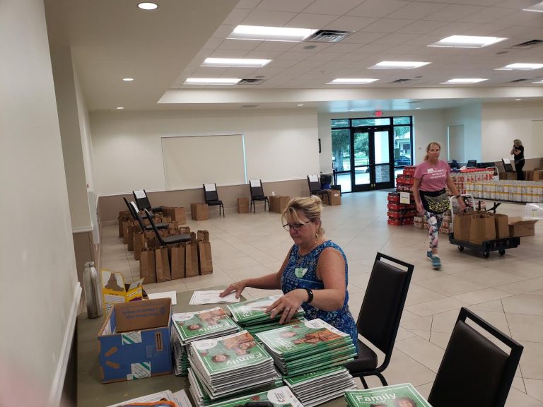 Volunteer seated at a table stacking Family Resource Guides in a meeting hall