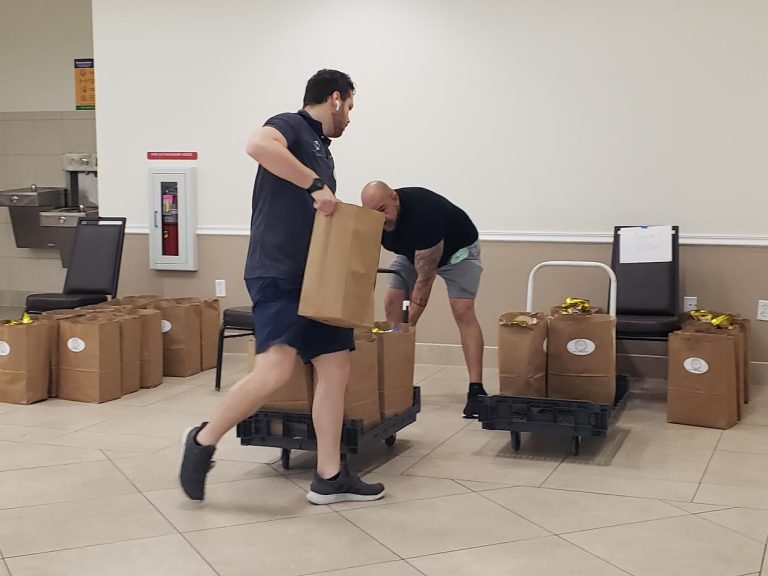 Two volunteers lifting packed grocery bags onto carts along a hallway