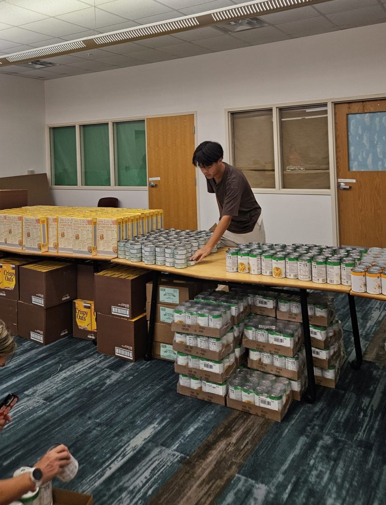 Teen arranging canned goods on long tables in a classroom at Monthly Packings