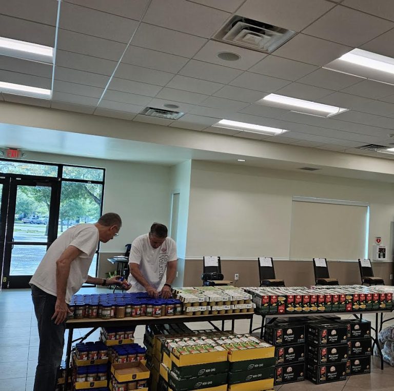 Two volunteers arranging canned goods on tables by the windows