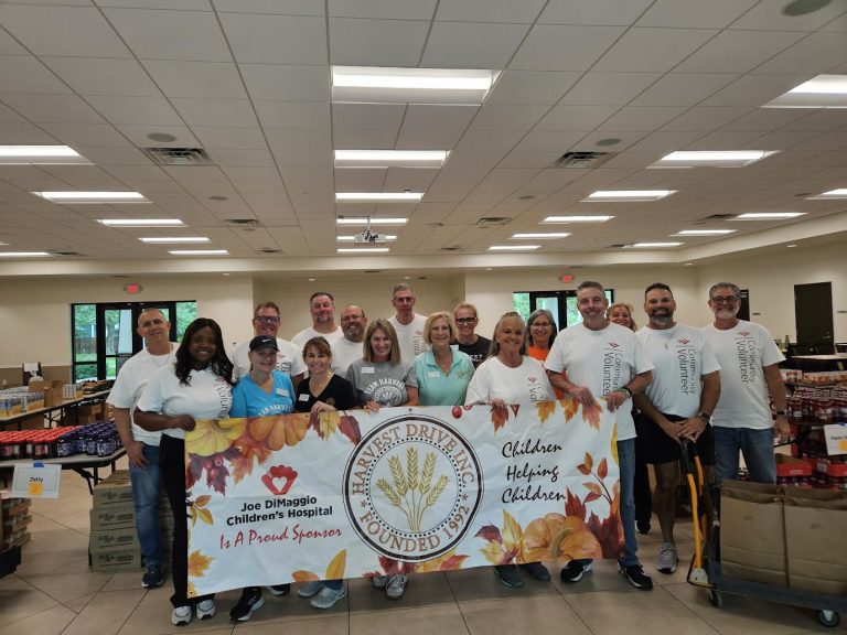Large volunteer group behind a Harvest Drive Children Helping Children banner at Monthly Packings