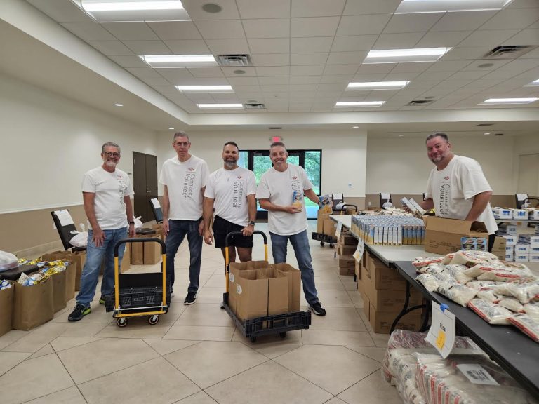 Volunteers with carts and boxes posing among tables of food at Monthly Packings