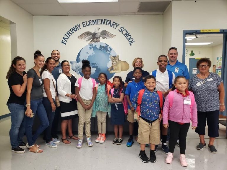 Children with new backpacks and adults posing beneath a "Fairway Elementary School" eagle mural