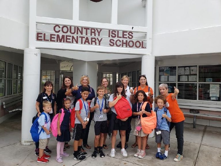 Children wearing new backpacks posing with adults outside under the Country Isles Elementary School sign
