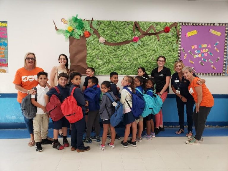 Country Isles Elementary School students with new backpacks posing in front of a tree bulletin board