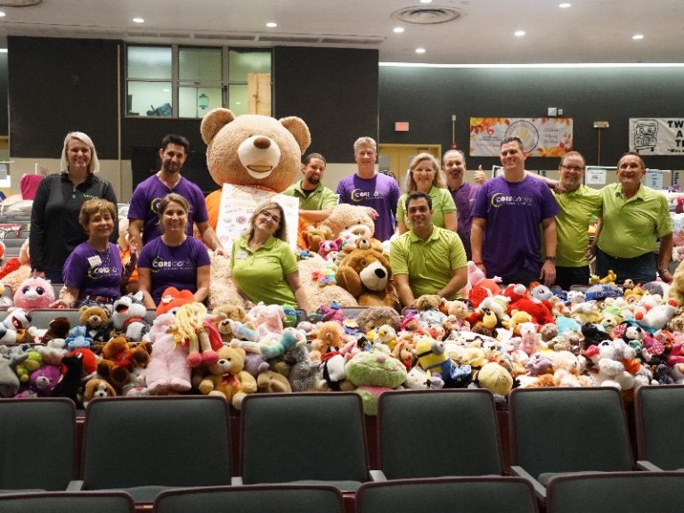 Volunteers in matching shirts behind piles of plush toys and a giant teddy bear in the school auditorium