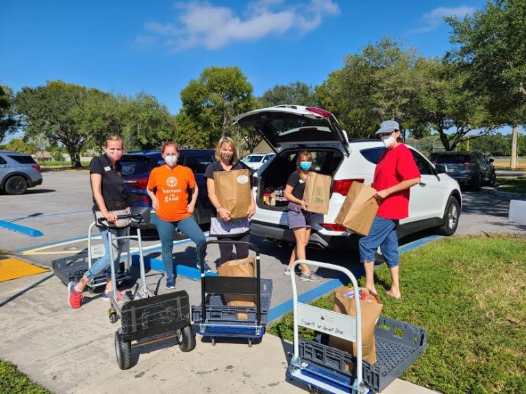 Masked volunteers with hand carts carrying grocery bags to an SUV at Monthly Bag Packings