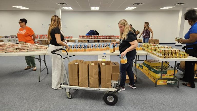 Volunteers filling bags on a large cart between tables of canned food at Monthly Packings