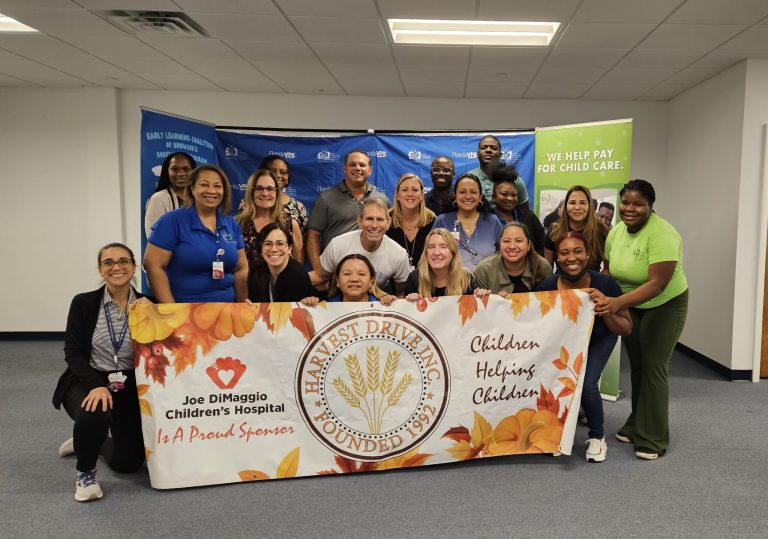 Volunteers with a Harvest Drive banner in front of an Early Learning Coalition backdrop at Monthly Packings