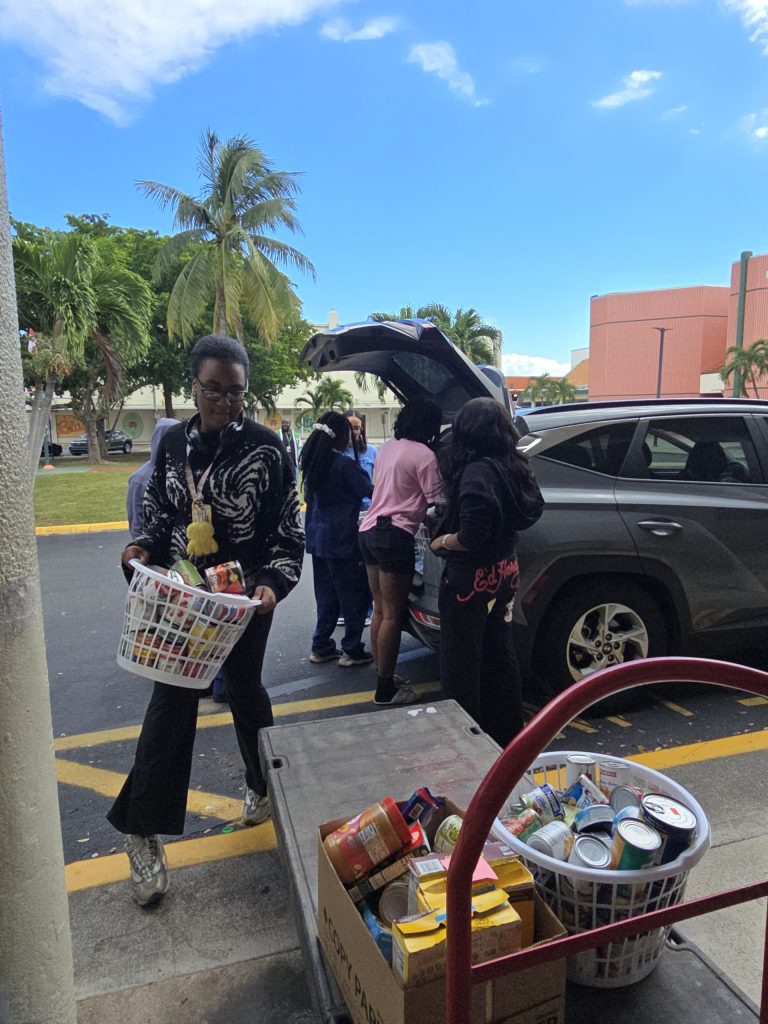 Blanche Ely High School students carrying baskets of food from a car to a cart in the school parking lot