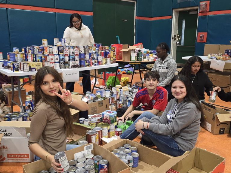 Blanche Ely High School students sitting among boxes and tables stacked high with canned food in the gym