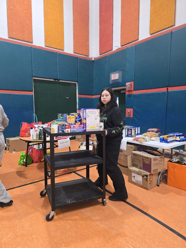 Blanche Ely High School student standing beside a rolling cart of food in the gym