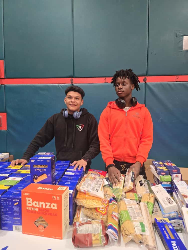 Two Blanche Ely High School students behind a table of pasta boxes and bags of rice