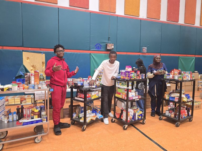 Blanche Ely High School students posing beside rolling carts loaded with food in the gym