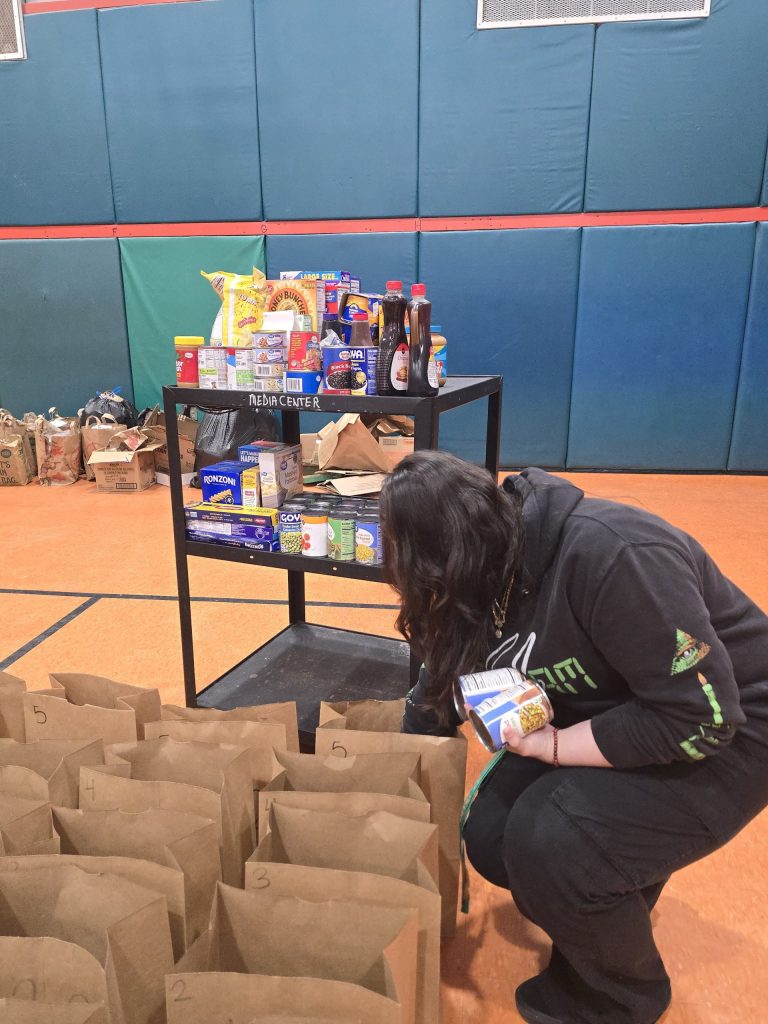 Blanche Ely High School student crouching to fill paper grocery bags beside a food cart