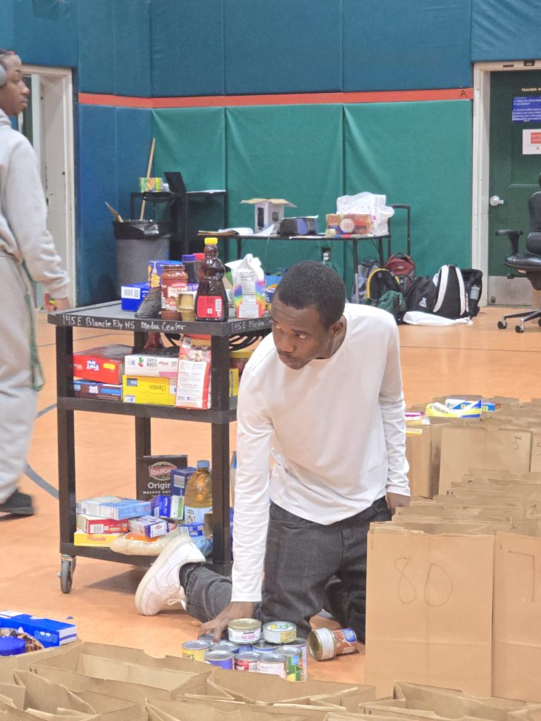 Blanche Ely High School student kneeling to pack paper grocery bags next to a loaded cart