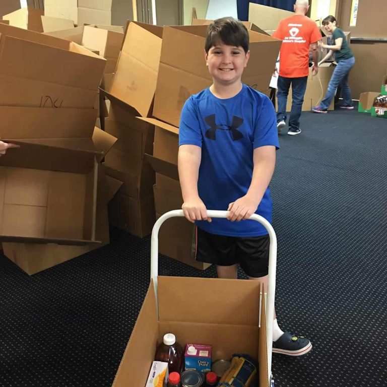 Child pushing a hand truck carrying a box of groceries at the Box Packing Program