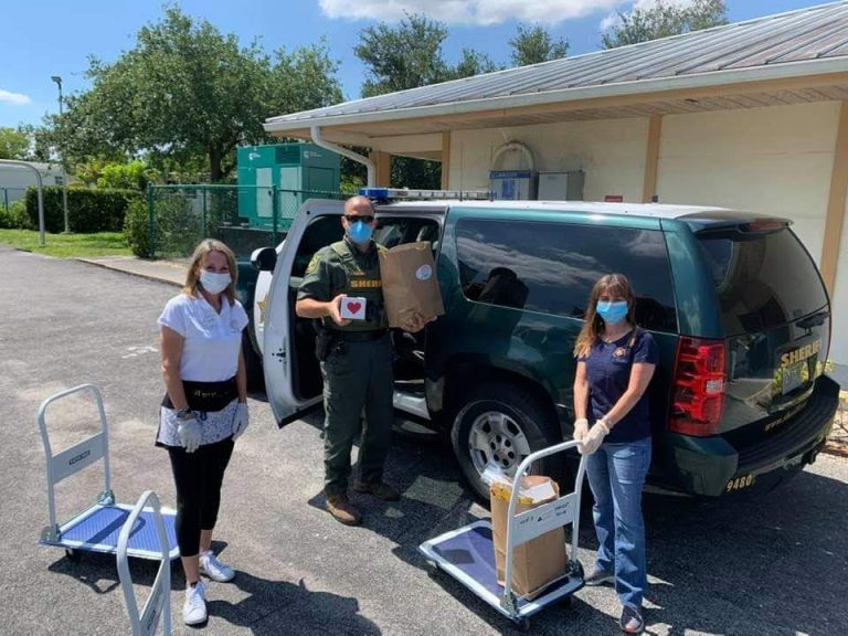 Masked volunteers with hand carts beside an SUV loaded with grocery bags at Monthly Bag Packings