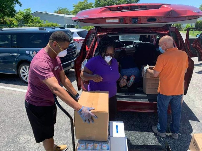 Masked volunteers loading a cardboard box into a red SUV at Monthly Bag Packings