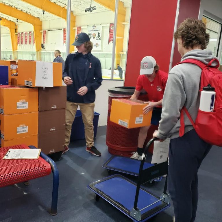 Teens moving boxes of food onto a cart in a rink lobby