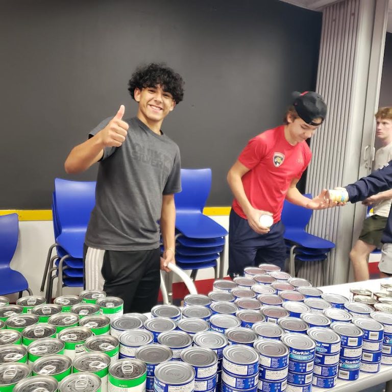 Teen giving a thumbs-up beside tables of canned vegetables and tuna