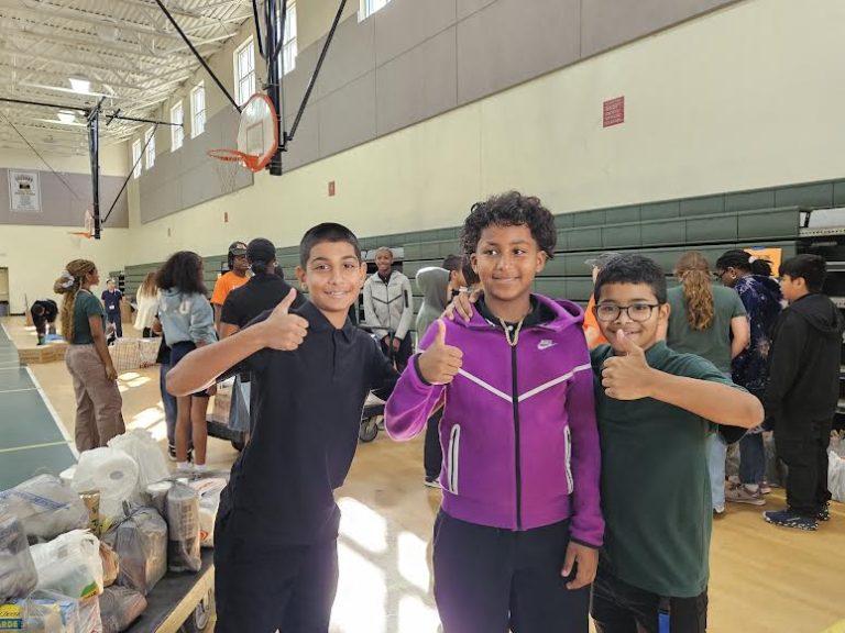 Three Glades Middle School students giving thumbs up in the gym beside donated food