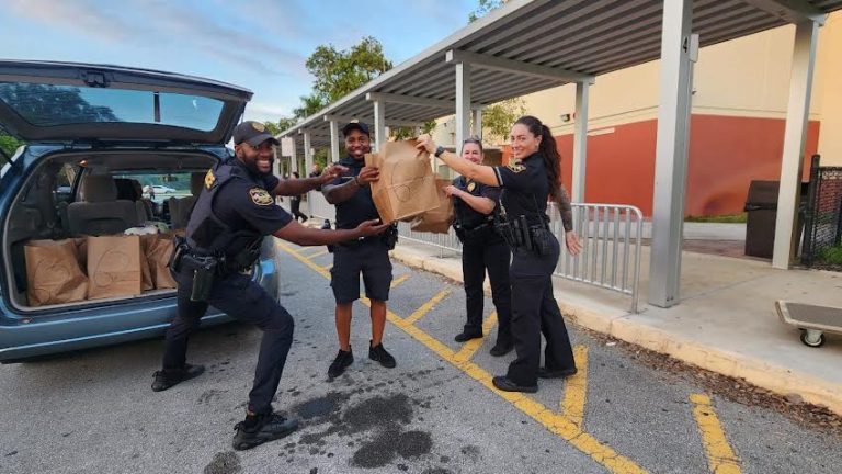 Police officers and volunteers loading grocery bags into an SUV during the Glades Middle School food drive pickup