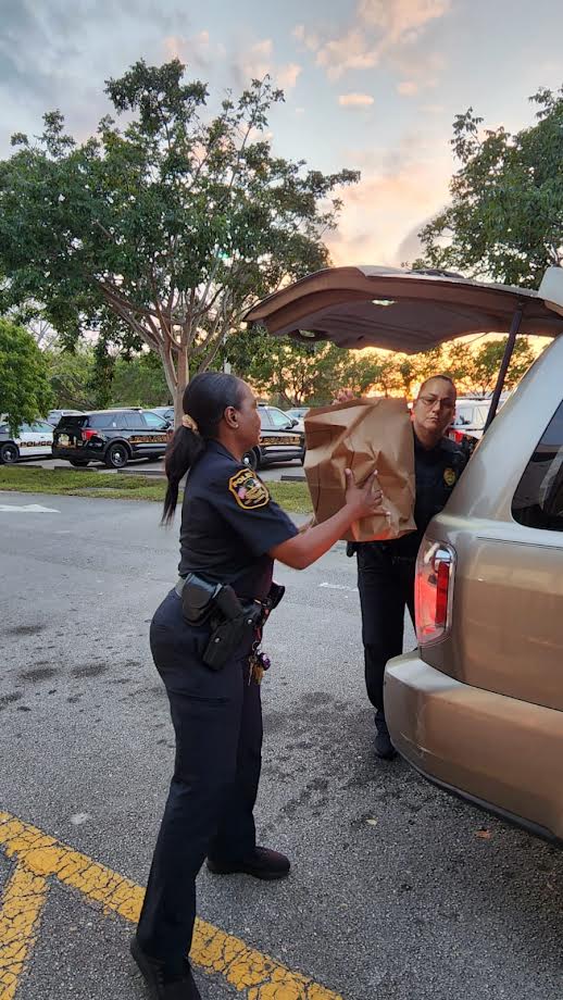 Glades Middle School officer handing a grocery bag toward an open SUV at sunset