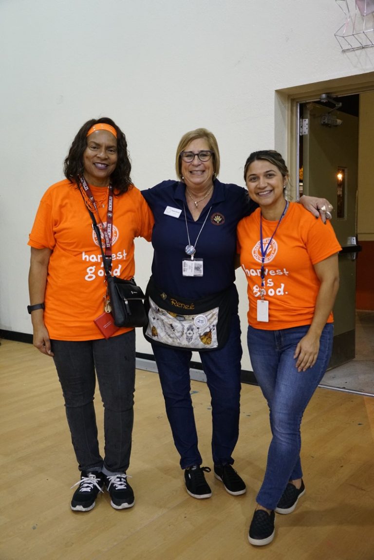 Three Glades Middle School volunteers in orange and navy shirts posing together indoors