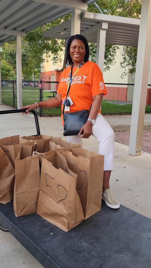 Glades Middle School volunteer in an orange shirt standing behind a cart of labeled grocery bags