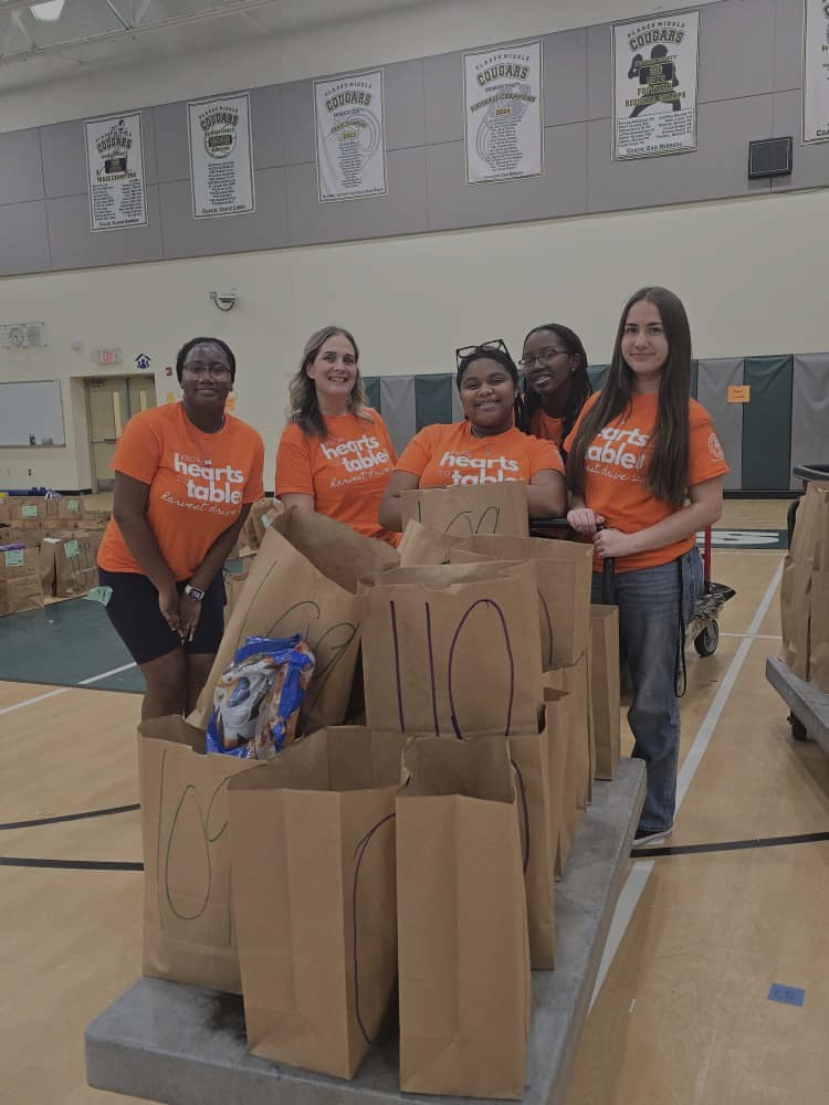 Glades Middle School students and staff in orange shirts behind numbered grocery bags in the gym