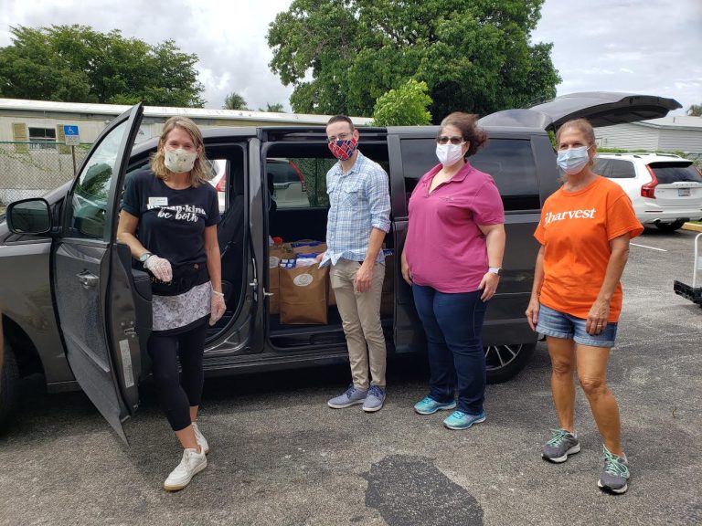 Masked volunteers standing beside a van with an open side door full of bags at Monthly Bag Packings