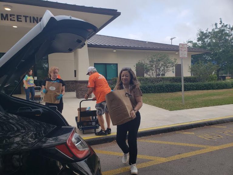 Volunteers carrying grocery bags from carts to an open hatchback at Monthly Packings