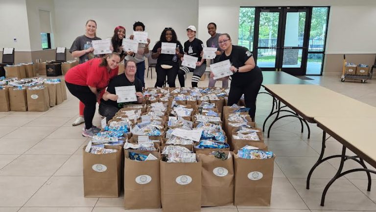 Volunteers holding certificates behind rows of filled grocery bags on the floor
