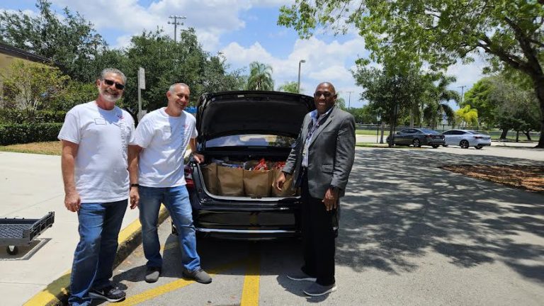 Volunteers beside a car trunk loaded with grocery bags outdoors at Monthly Packings