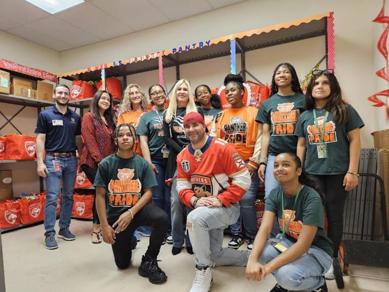 Students and Florida Panthers staff posing in a school pantry stocked with red tote bags