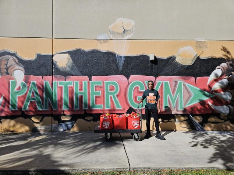 Student with a cart of red tote bags in front of a large Panther Gym mural