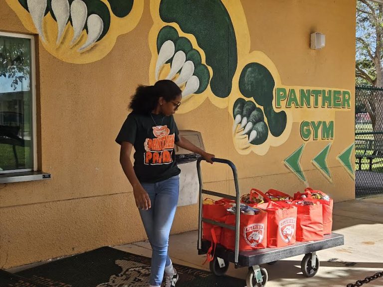 Student pulling a cart of red tote bags past a Panther Gym mural