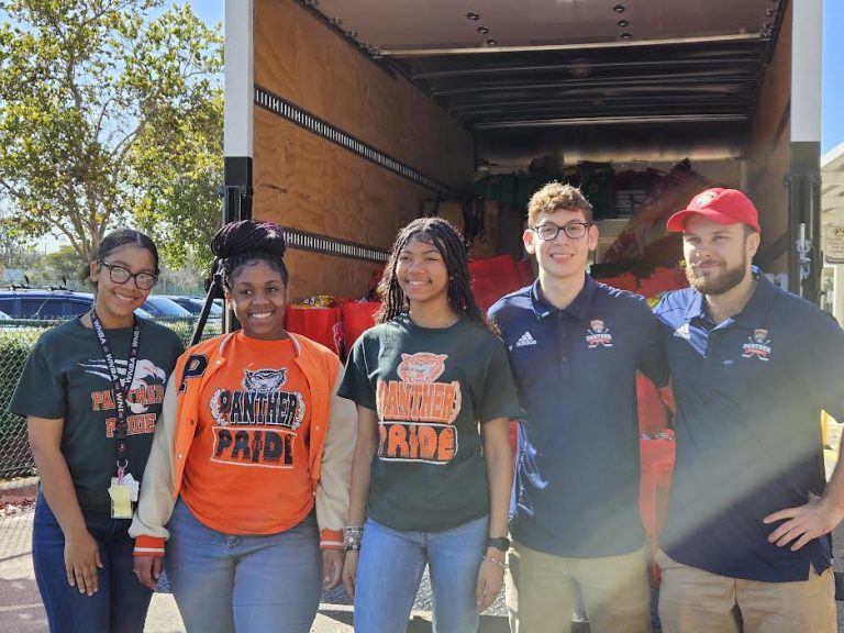 Students and Florida Panthers staff in front of a truck loaded with red tote bags