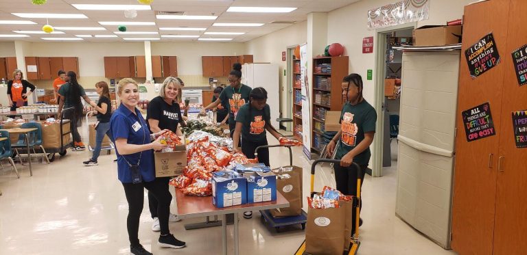 Volunteers and students with carts of grocery bags between snack tables at Monthly Packings