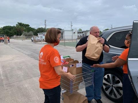 Pompano Beach High School volunteers handing a bag of food to a driver beside his car