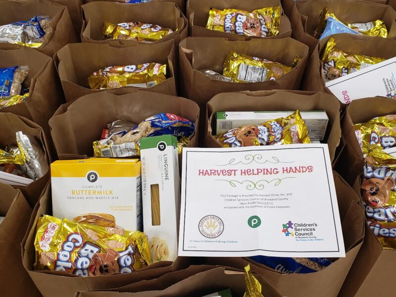 Overhead view of paper bags with cookies, pasta and pancake mix beside a Harvest Helping Hands sign