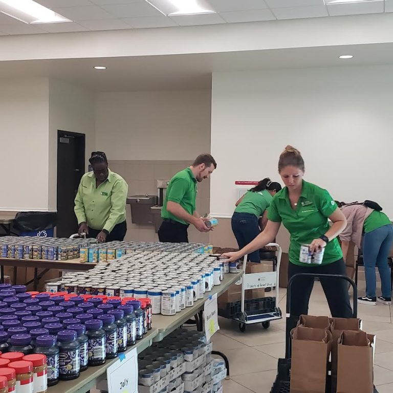 Publix volunteers in green shirts sorting jars and canned goods on long tables