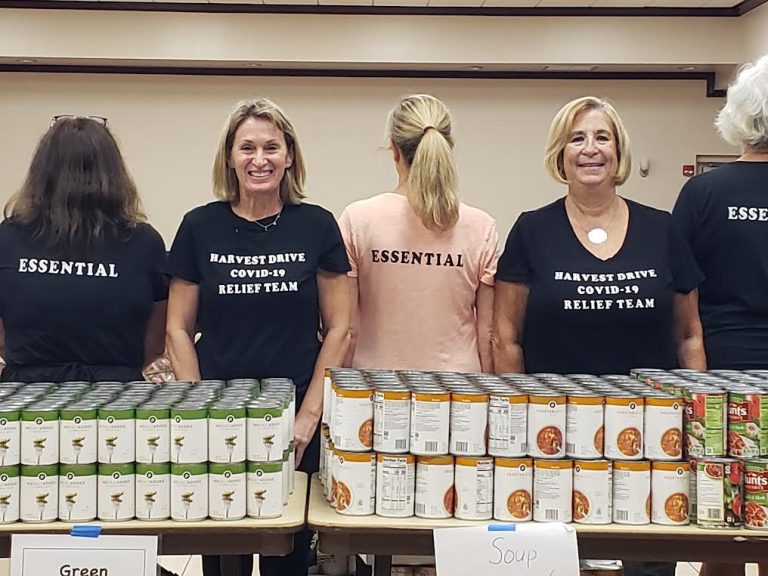 Volunteers in Harvest Drive COVID-19 Relief Team shirts stand behind rows of canned soup