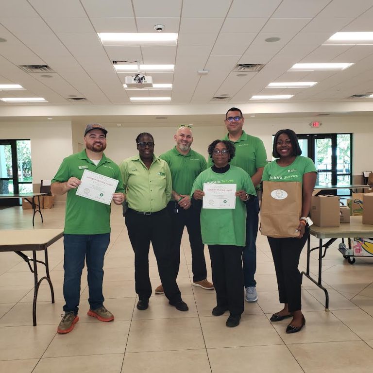 Publix volunteers in green shirts holding certificates in a meeting hall
