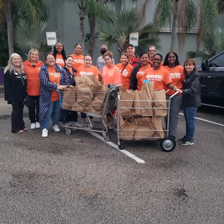 Stranahan High School volunteers in orange shirts posing with carts of filled grocery bags in a parking lot