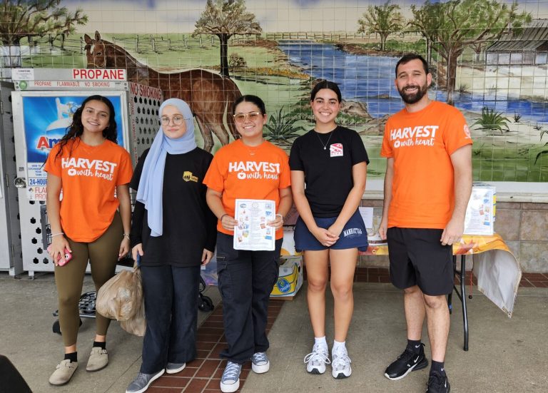 Western High School volunteers in orange Harvest shirts at a collection table in front of a painted mural