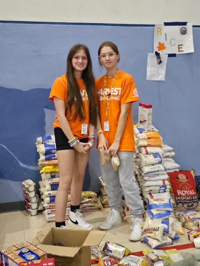 Two Westglades Middle School students standing beside piles of rice bags and boxed food
